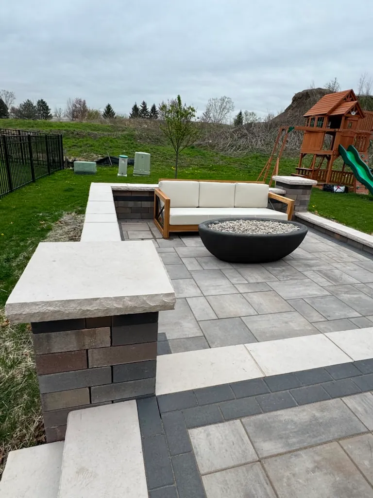 Multi-tone paver patio with seat walls, capped columns, teak seating, and a modern black fire bowl in Chicago's Southwest Suburbs