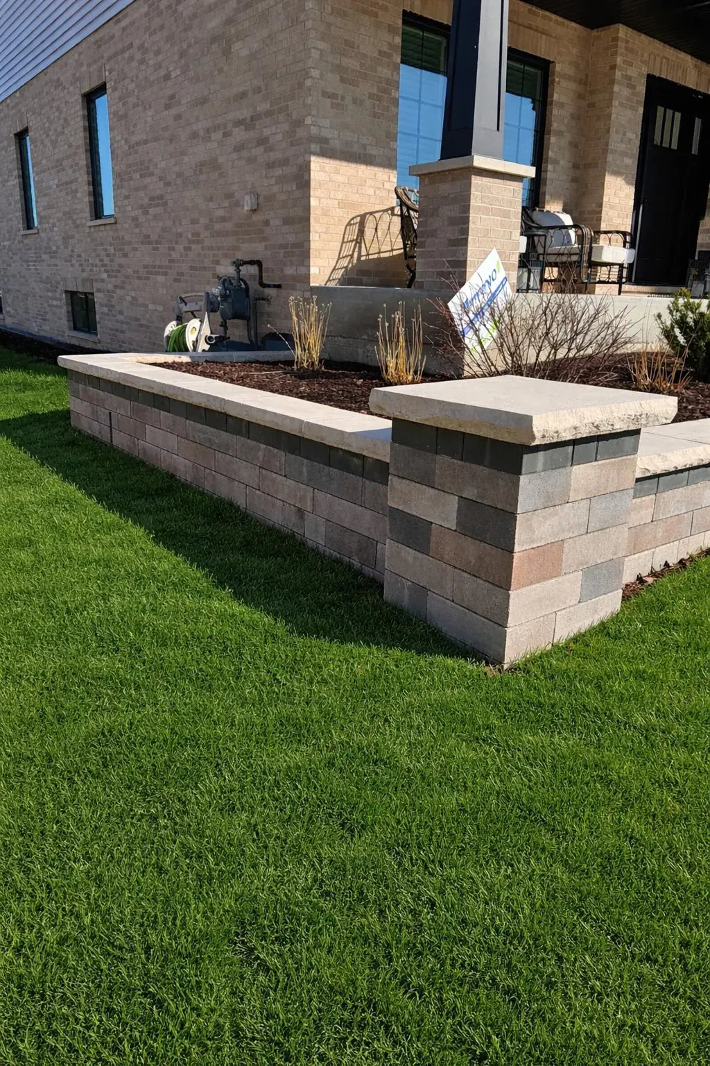Tan and brown paver seat wall with smooth cap stones bordering a raised mulch planter in Chicago's Southwest Suburbs